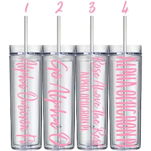 May include: Four clear plastic tumblers with pink lettering. The tumblers have straws and are labeled "Go Alpha O", "Rose Above The Rest", "Alpha Omicron Pi", and "Alpha Omicron Delta".