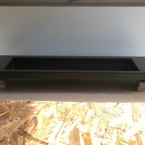 Puede incluir: Un lavabo rectangular negro con un borde elevado, apoyado en bloques de madera. El lavabo est&aacute; hecho de un material liso y s&oacute;lido.