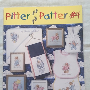May include: A Pitter Patter #4 cross-stitch pattern booklet by Jeanette Crews Designs featuring various baby-themed embroidery projects including framed art, a hooded towel, a bib, and a gift bag, all decorated with illustrations of infants.