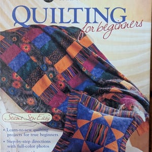 May include: A book cover titled "QUILTING for beginners" by Coats & Clark. The cover features a colorful quilt with blue, orange, and purple squares. A matching pillow with an orange star design is also visible. The book promises step-by-step directions and a guide to fabrics.