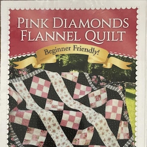 May include: A pattern booklet titled Pink Diamonds Flannel Quilt with the text Beginner Friendly on a gold ribbon. The cover features a quilt with a black background, pink and white checkered squares, and floral fabric strips in a diamond layout.