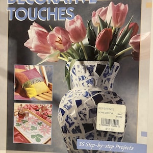 May include: A book cover titled "DECORATIVE TOUCHES" featuring a mosaic vase filled with pink and red tulips. The vase is white with blue mosaic tiles. Additional images show a pillow, a tray, and a decorative object.