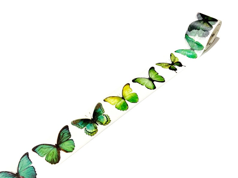 May include: A roll of washi tape with a repeating pattern of green, yellow, and blue butterflies. The butterflies are arranged in a line, with the largest butterfly at the end of the roll.