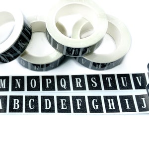 May include: Black and white alphabet washi tape rolls with letters printed in white on black squares. The tape is unrolled to show the letters LMNOPQRSTUV and ZABCDEFGHIJ.