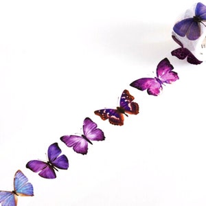 May include: A roll of washi tape with a repeating pattern of purple, pink, and blue butterflies. The tape is on a white background.