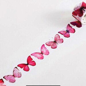 May include: Pink and red butterfly patterned washi tape. The tape is unrolled and shows a row of butterflies in various shades of pink and red.