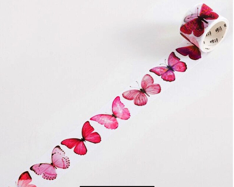 May include: Pink and red butterfly patterned washi tape. The tape is unrolled and shows a row of butterflies in various shades of pink and red.