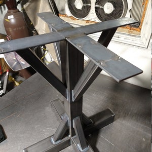 May include: A metal table base with a square top and four legs. The legs are welded together in a cross shape, and the base is made of thick, sturdy metal.
