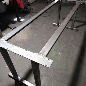 May include: A metal table frame with two legs and a rectangular top. The frame is made of square metal tubing and has a welded construction.