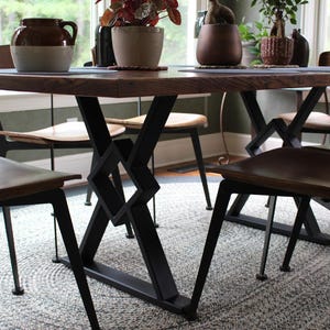 May include: A dark wood dining table with a black metal X-shaped base. The table is surrounded by four chairs with brown wooden seats and black metal frames.