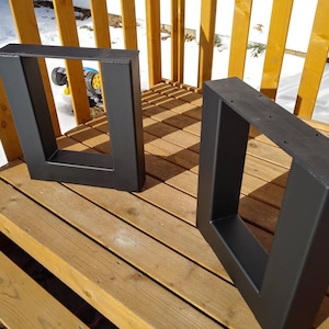 May include: Two black metal table legs with a square frame. The legs are made of thick metal and have a matte black finish.