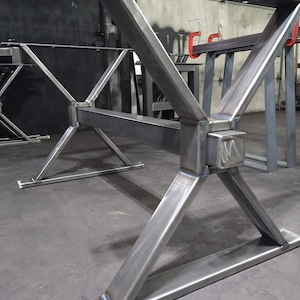 May include: A metal table base with an X-shaped design. The base is made of thick, welded steel and has a gray finish.