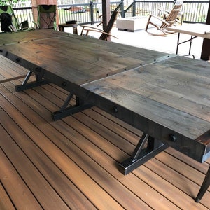 Pu&ograve; includere: Un lungo tavolo da pranzo rettangolare con un piano in legno tinto scuro composto da pi&ugrave; assi. Il tavolo &egrave; rinforzato con bordi in metallo nero fissati con bulloni a vista. Poggia su tre basi a cavalletto in metallo nero.