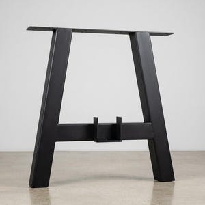 May include: A matte black metal table leg frame featuring two angled vertical supports connected by a horizontal crossbar. The top includes a flat mounting plate with pre-drilled holes, and the center of the crossbar features a U-shaped bracket.