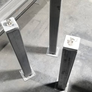 May include: Three silver metal table legs with square bases. The legs are standing on a gray concrete floor.