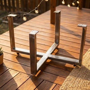 May include: A silver-colored metal table base featuring a cross-shaped design with four vertical supports. Each vertical support has a flat rectangular mounting plate at the top with four pre-drilled holes for attachment to a tabletop surface.