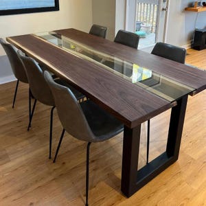 May include: A dark wood dining table with a glass top insert and black metal legs. The table is set with four chairs.