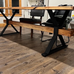 May include: A wooden dining table with a live edge top and black metal X-shaped legs. The table is in a room with hardwood floors.