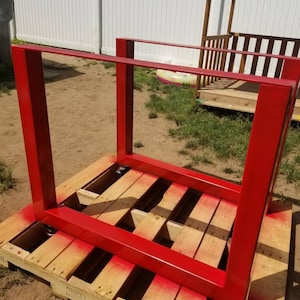 May include: Red metal table legs on a wooden pallet. The legs are square and have a simple design. The pallet is made of wood and has a weathered look.