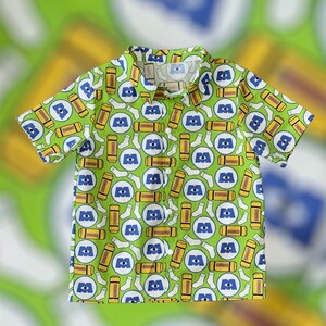 May include: A green short-sleeved button-down shirt with a repeating pattern of blue eyes and yellow socks. The shirt has a white collar and white buttons.