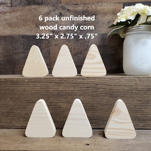 May include: Six unfinished wooden triangle shapes, resembling candy corn, measuring 3.25 inches by 2.75 inches by 0.75 inches. The triangles are arranged in two rows of three on a wooden surface.