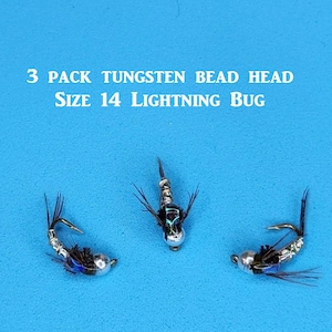 May include: Three tungsten bead head fishing flies, size 14 Lightning Bug, are displayed against a bright blue background. The flies have silver bodies, black accents, and blue highlights, with small hooks and delicate black fibers.