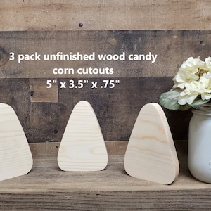May include: Three unfinished wooden candy corn cutouts, each measuring 5 inches by 3.5 inches by 0.75 inches. The cutouts are arranged in a row on a wooden surface.