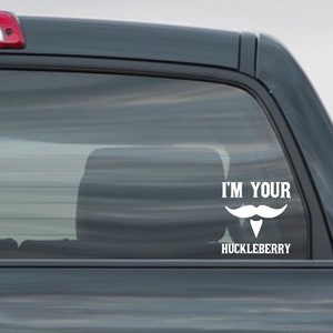 May include: A white vinyl sticker with the text "I'm Your Huckleberry" and a white mustache and goatee design on a gray truck window.