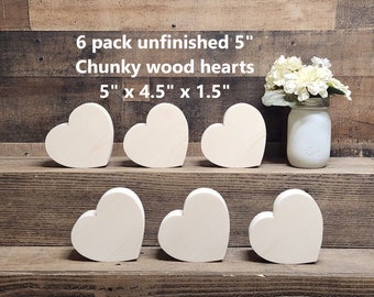 May include: Six unfinished wooden hearts in the shape of a heart. The hearts are 5 inches by 4.5 inches by 1.5 inches. They are arranged in two rows of three on a wooden surface.