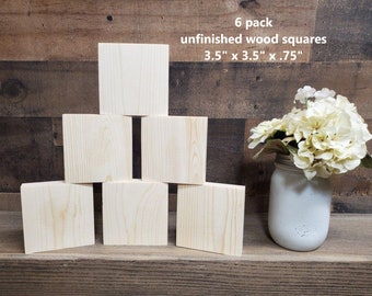 May include: Six unfinished wood squares, each measuring 3.5 inches by 3.5 inches by 0.75 inches. The squares are stacked in a pyramid shape on a wooden surface. A bouquet of white flowers is in a white jar to the right of the squares.
