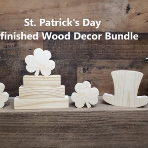 May include: Unfinished wood decor bundle for St. Patrick's Day. The bundle includes three shamrock shapes, a stack of three wooden blocks, and a leprechaun hat.