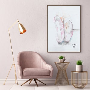 Puede incluir: Una pintura de acuarela de dos zapatillas de ballet rosas con cintas blancas. La pintura está enmarcada y colgada en una pared en una habitación con un sillón rosa, una lámpara de pie dorada y dos mesas auxiliares doradas.