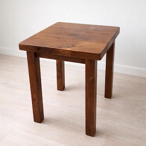 May include: A small, square wooden table with a rich brown finish. The table has a simple design with four sturdy legs and a flat top. The table's dimensions are approximately 46 cm in height and 41 cm wide.