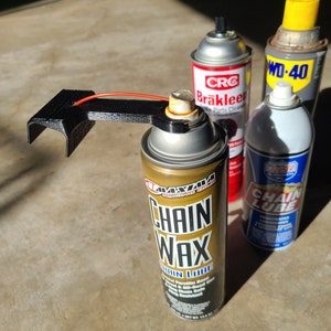 Pu&ograve; includere: Tre bombolette spray, una nera, una rossa e bianca e una blu e bianca, con il testo "CRC Brakleer Parts Cleaner", "WD-40" e "Chain Lube" su di esse. Una bomboletta spray dorata con il testo "Chain Wax" &egrave; al centro dell'immagine.