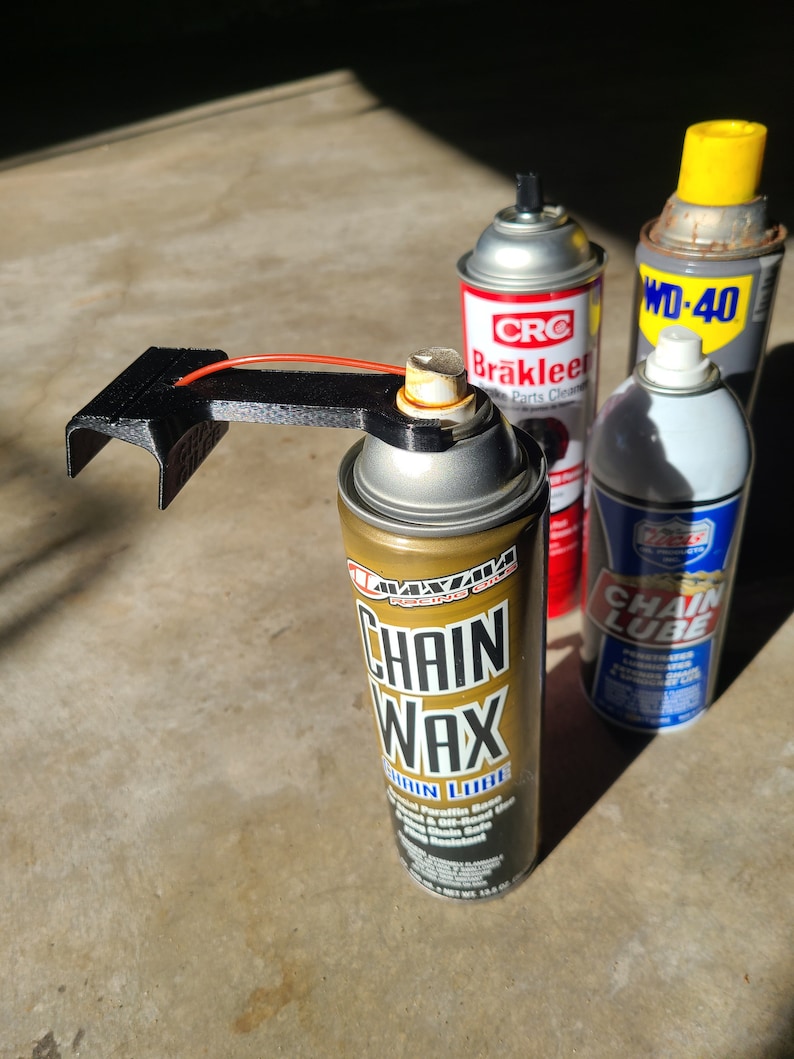 Pu&ograve; includere: Tre bombolette spray, una nera, una rossa e bianca e una blu e bianca, con il testo "CRC Brakleer Parts Cleaner", "WD-40" e "Chain Lube" su di esse. Una bomboletta spray dorata con il testo "Chain Wax" &egrave; al centro dell'immagine.