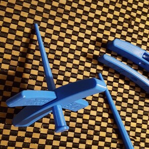 Peut inclure: Une roue &agrave; filer en plastique bleue avec quatre bras et une broche. La roue est sur une surface &agrave; carreaux noirs et bruns.