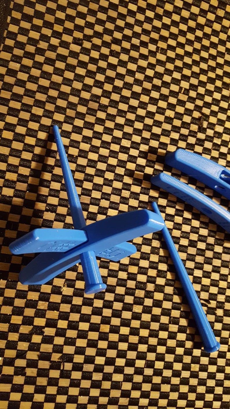 Peut inclure: Une roue &agrave; filer en plastique bleue avec quatre bras et une broche. La roue est sur une surface &agrave; carreaux noirs et bruns.