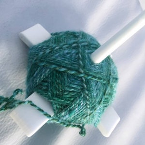 Peut inclure: Un enrouleur de laine blanc avec une pelote de laine turquoise et verte enroul&eacute;e autour.