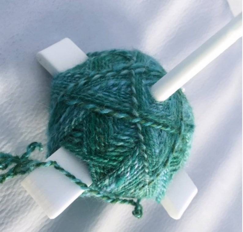 Peut inclure: Un enrouleur de laine blanc avec une pelote de laine turquoise et verte enroul&eacute;e autour.