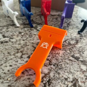 Pu&ograve; includere: Uno strumento in plastica arancione brillante con un logo bianco. Lo strumento ha un manico e due punte. &Egrave; progettato per aiutare ad aprire le cose.