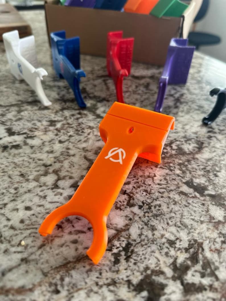 Pu&ograve; includere: Uno strumento in plastica arancione brillante con un logo bianco. Lo strumento ha un manico e due punte. &Egrave; progettato per aiutare ad aprire le cose.