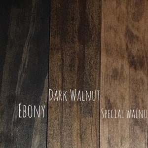 May include: A close-up of three wood stain samples: Ebony, Dark Walnut, and Special Walnut. The names of the stains are written in white script. The wood grain is visible in each sample, showcasing the different tones of brown.