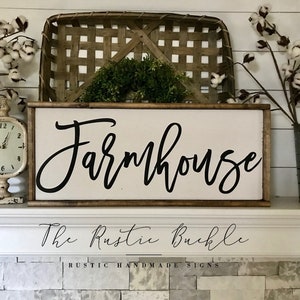 May include: A wooden sign with the word "Farmhouse" in black cursive script. The sign has a dark brown frame and a white background. The text "The Rustic Buckle" and "RUSTIC HANDMADE SIGNS" are also visible.