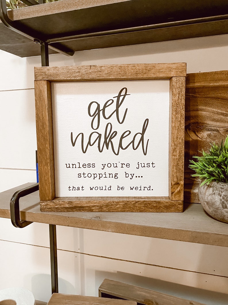 May include: Square wooden sign with a white background and the words "get naked" in a black, cursive font. Below, the text continues, "unless you're just stopping by... that would be weird."