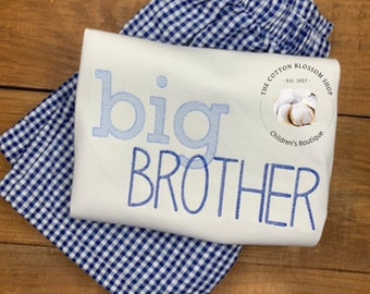 May include: A white t-shirt with blue embroidery that says "big brother". The shirt is paired with blue and white gingham shorts. The t-shirt also has a small circular logo that says "The Cotton Blossom Shop - Est. 2017 - Children's Boutique".