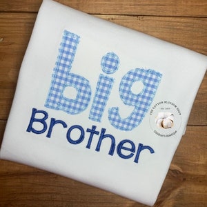 May include: White shirt with the words "Big Brother" embroidered in blue. The word "big" is in a blue and white gingham pattern. The Cotton Blossom Shop logo is in the lower right corner.