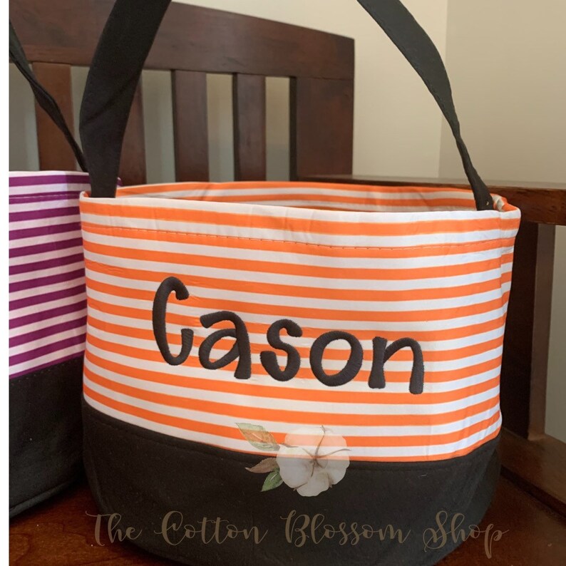May include: Orange and white striped Halloween trick-or-treat bucket with black handles and a black bottom. The bucket is personalized with the name "Gason" in black embroidery.