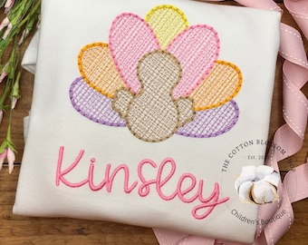 May include: A white babygrow with a pink embroidered turkey design and the name "Kinsley" in pink. The babygrow has a small logo in the bottom right corner that says "The Cotton Blossom Shop - Est. 2017 - Children's Boutique."