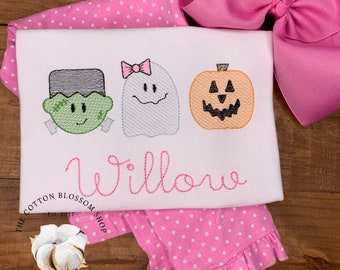 May include: White onesie with embroidered images of a ghost, a pumpkin, and Frankenstein. The onesie has the name "Willow" embroidered in pink below the images. The onesie is paired with pink polka dot leggings.