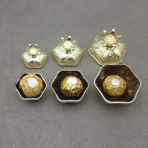 May include: Six gold-colored metal containers shaped like pomegranates. The containers are in various sizes and some have a chocolate truffle inside.